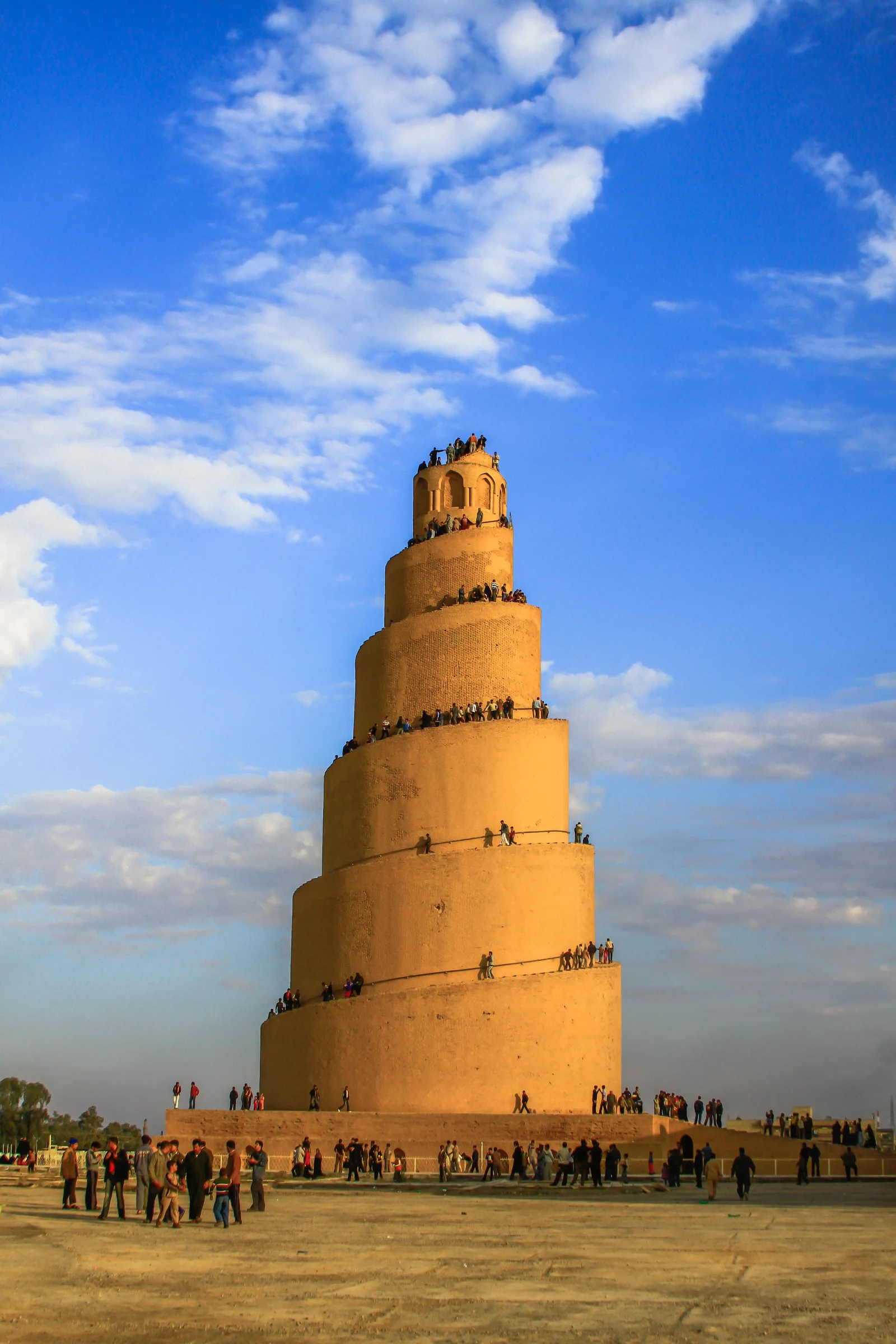 Des visiteurs gravissent la rampe en spirale du minaret Malwiya de Samarra, silhouettes visibles à plusieurs niveaux de la tour au coucher du soleil