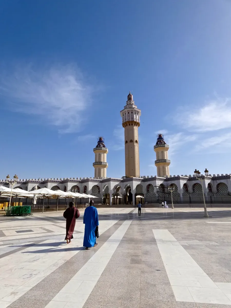 Deux visiteurs marchant vers les minarets de la Grande Mosquée de Touba sur l'esplanade