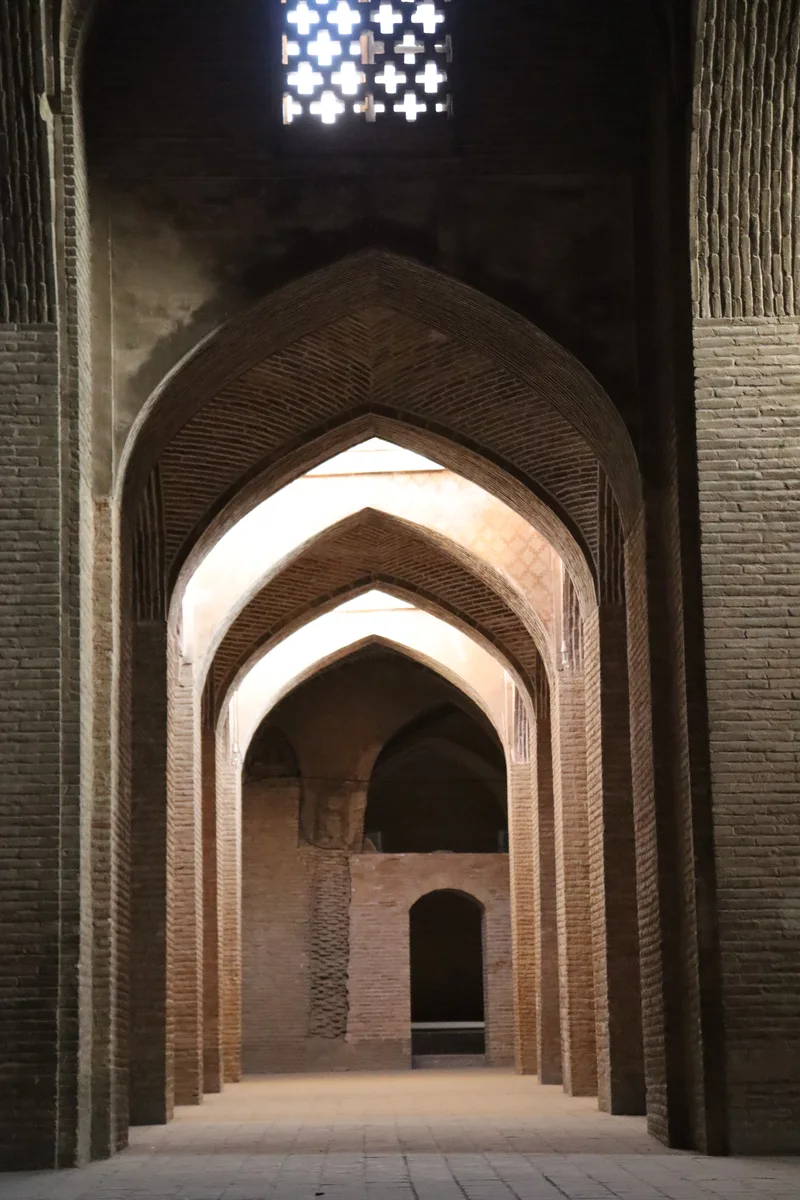 Galerie voûtée en brique de la Grande Mosquée du Vendredi d'Ispahan, éclairée par une fenêtre à claire-voie géométrique